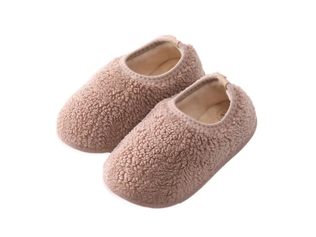 Ein Paar komfortable, hellrosa Kinderhausschuhe aus weichem Teddy-Stoff vor weißem Hintergrund.